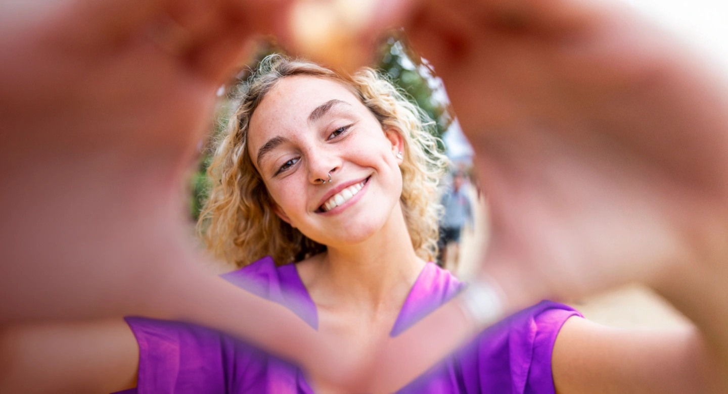 Happy woman making a heart shape with her hands, suggesting allergy relief and enjoying life outdoors.